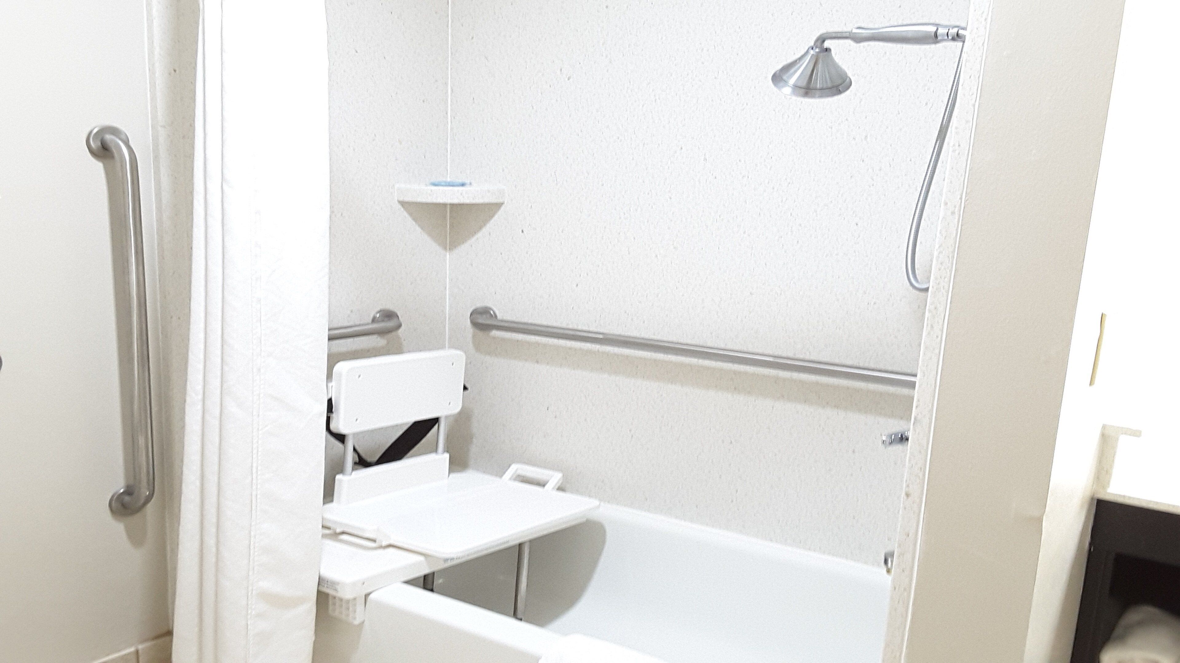Une salle de bain avec une baignoire blanche, une pomme de douche et une barre d’appui.