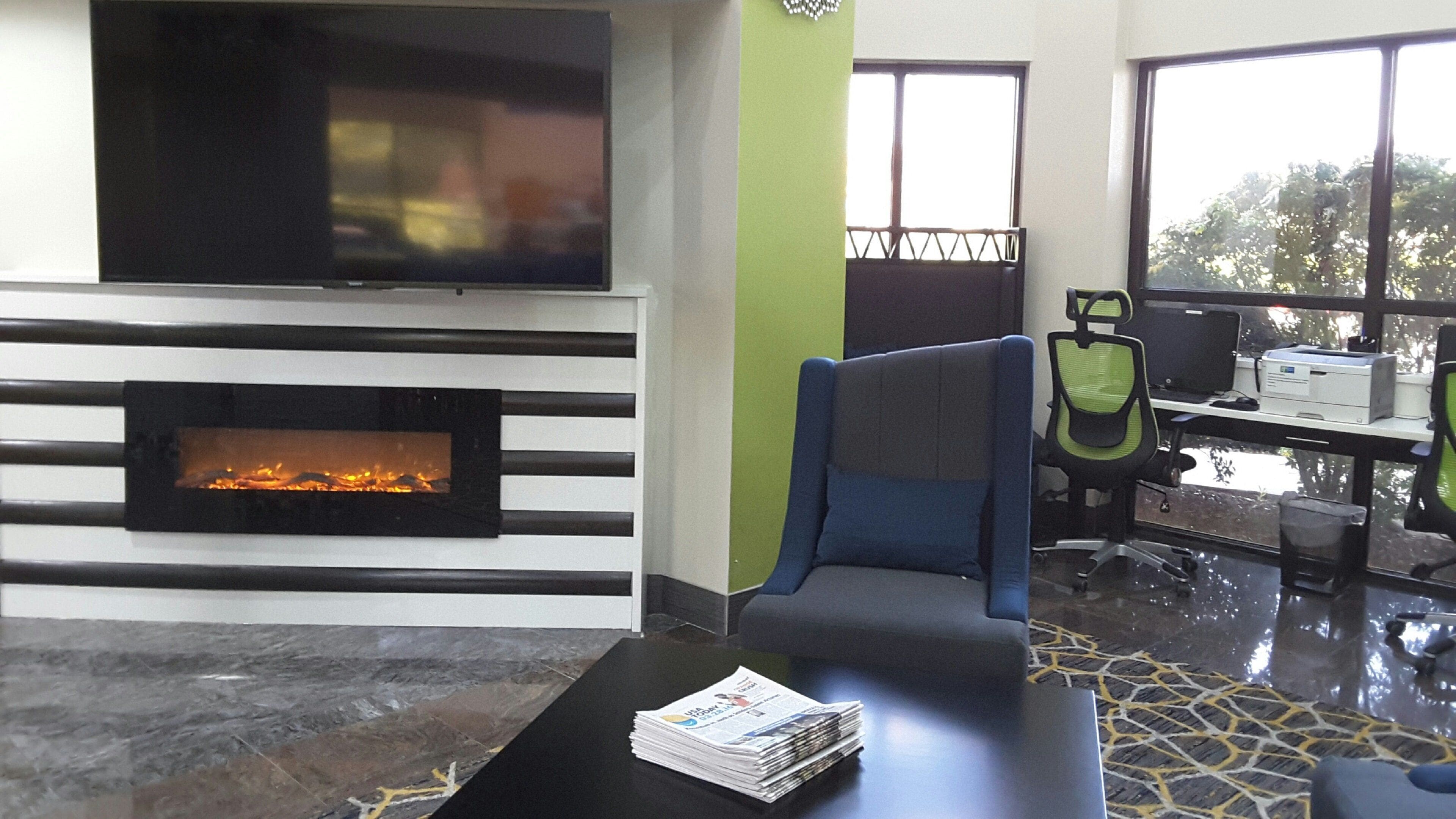 Ein modernes Wohnzimmer mit Kamin, einer Couch, einem Couchtisch mit Zeitungen und Blick ins Freie durch große Fenster.