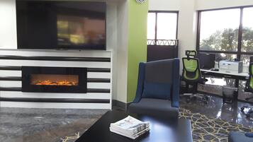 Ein modernes Wohnzimmer mit Kamin, einer Couch, einem Couchtisch mit Zeitungen und Blick ins Freie durch große Fenster.