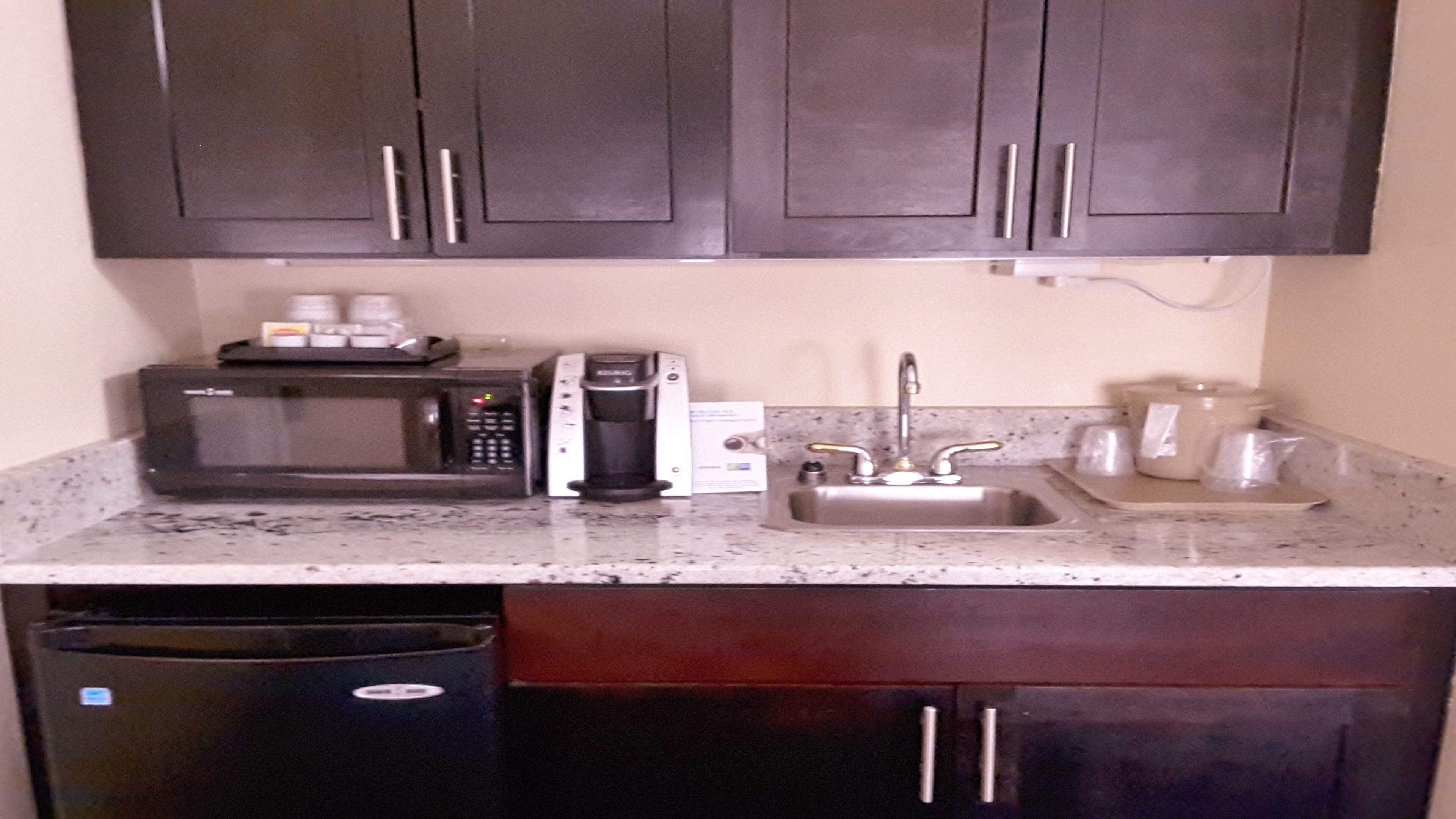 A kitchen with dark cabinets, a microwave, a coffee maker, a sink, and a dishwasher.