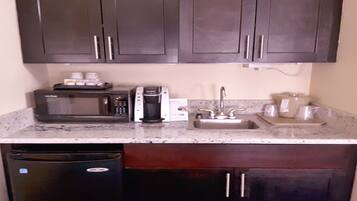 A kitchen with dark cabinets, a microwave, a coffee maker, a sink, and a dishwasher.