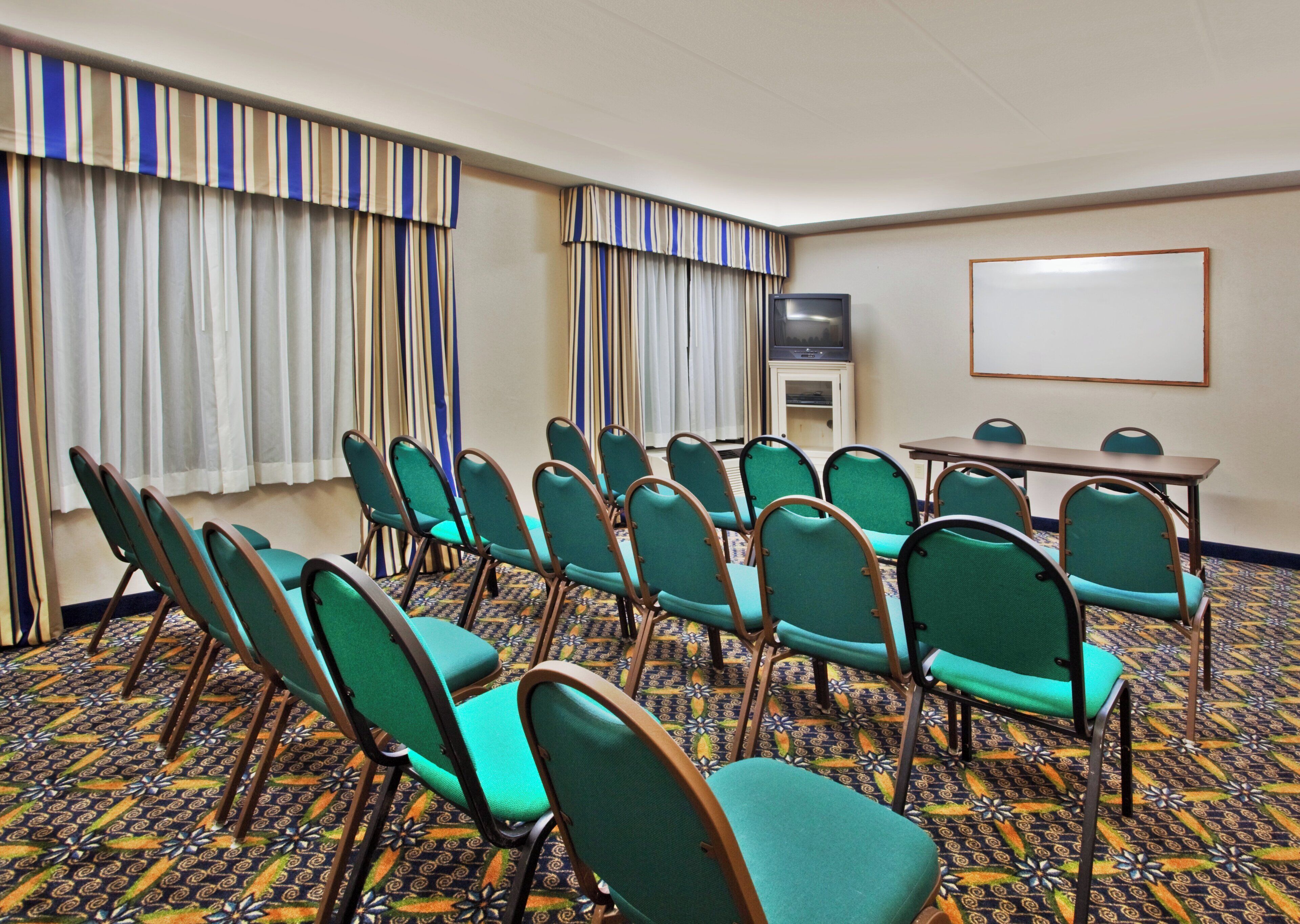 Une salle de conférence avec des rangées de chaises, un téléviseur et un tableau blanc.