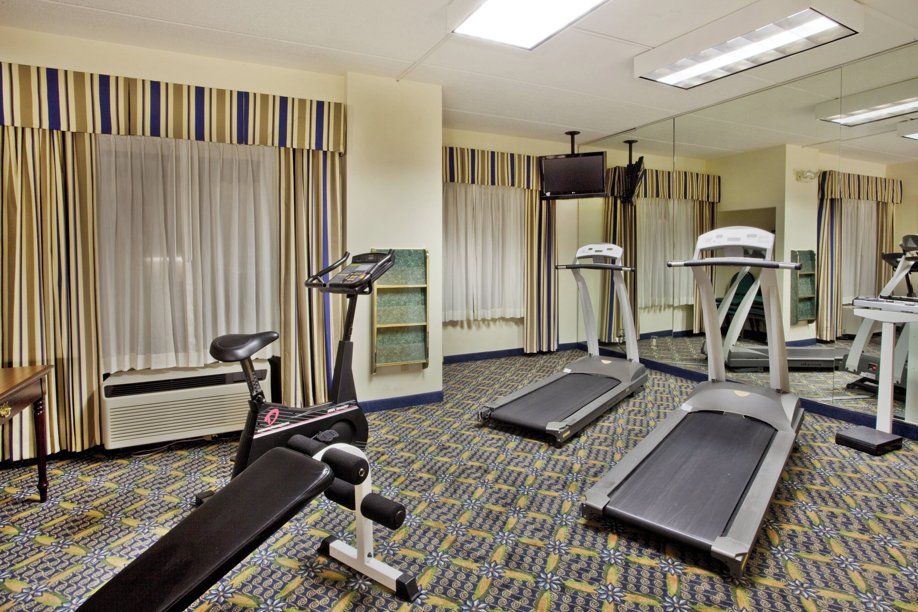 Une salle de sport d’hôtel équipée de matériel d’exercice, notamment un tapis de course, un vélo elliptique et un vélo d’appartement.