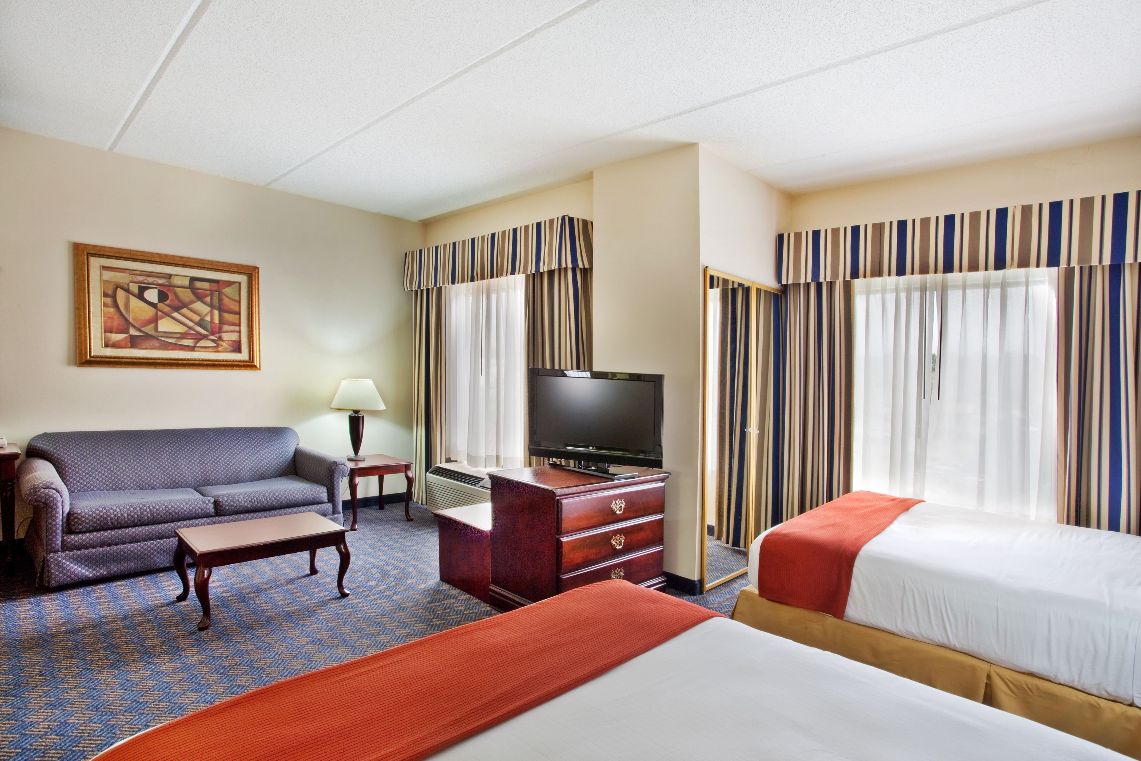 A hotel room with a sofa, a TV, a desk, and two beds.