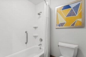 A bathroom with a white bathtub, a shower, a toilet, and a geometric wall art piece. - Comfort Inn & Suites Perry National Fairgrounds Area (Perry)