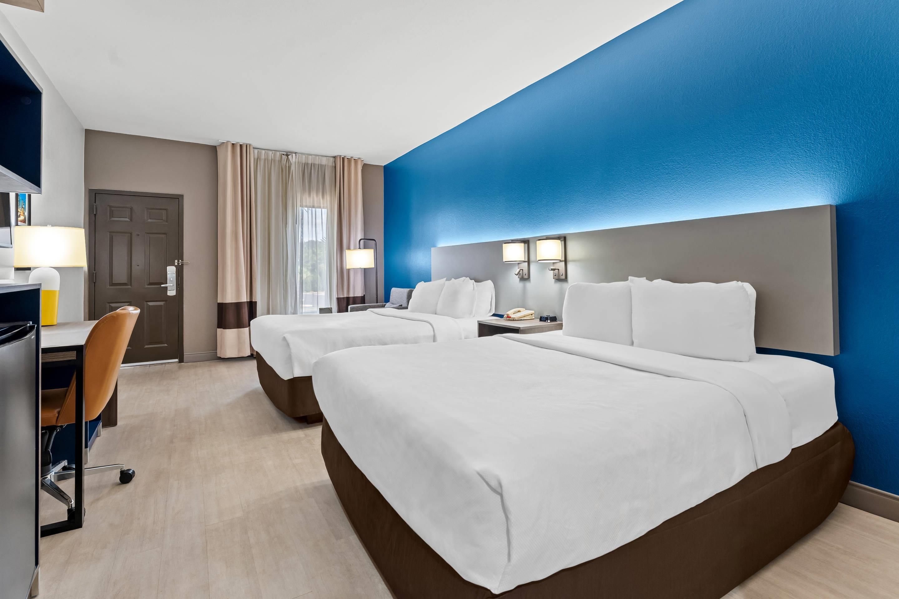 Ein Hotelzimmer mit zwei Betten, einem Schreibtisch, einem Stuhl und einem Fenster mit Vorhängen.
