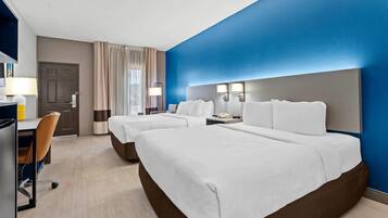 Ein Hotelzimmer mit zwei Betten, einem Schreibtisch, einem Stuhl und einem Fenster mit Vorhängen.
