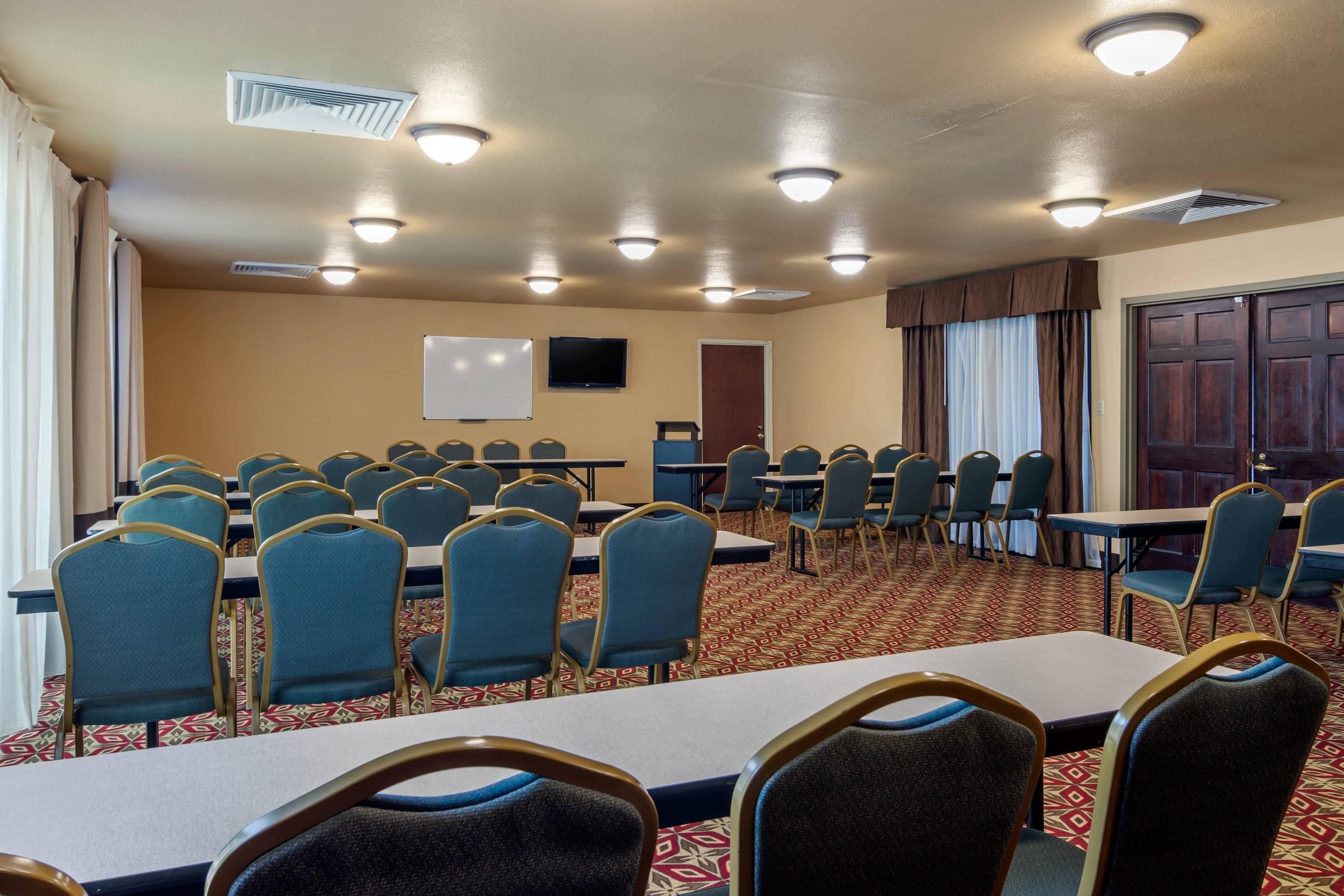 A conference room with tables and chairs, a whiteboard, a television, and a door.