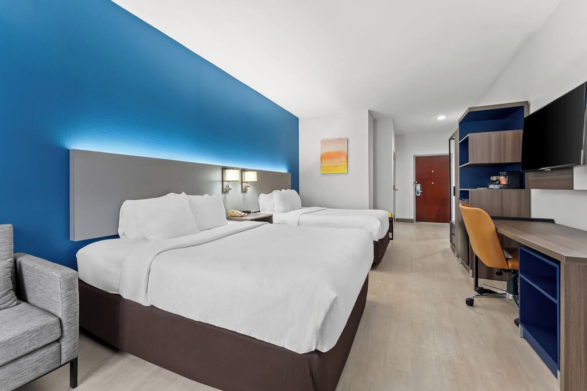 A hotel room with a large bed, two bedside tables, a desk with a chair, a TV, and a painting on the wall.