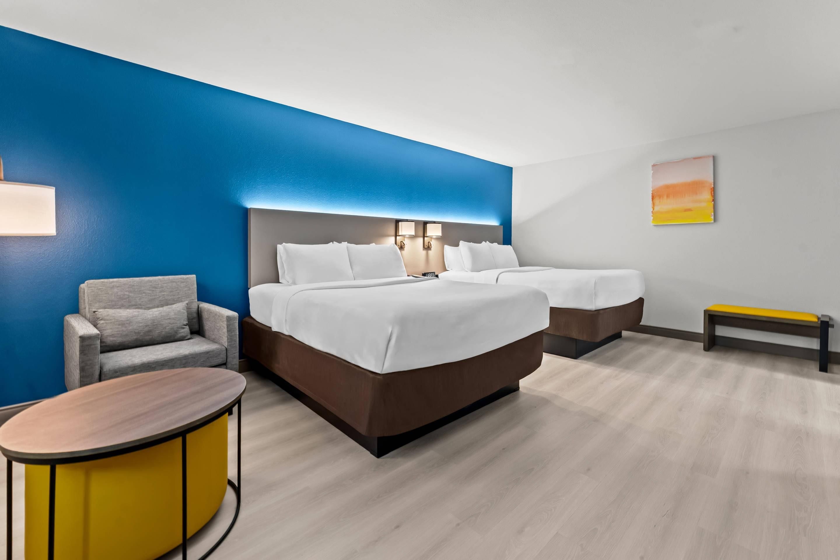 Una habitación de hotel con una cama grande, una silla, una mesita y un banco.