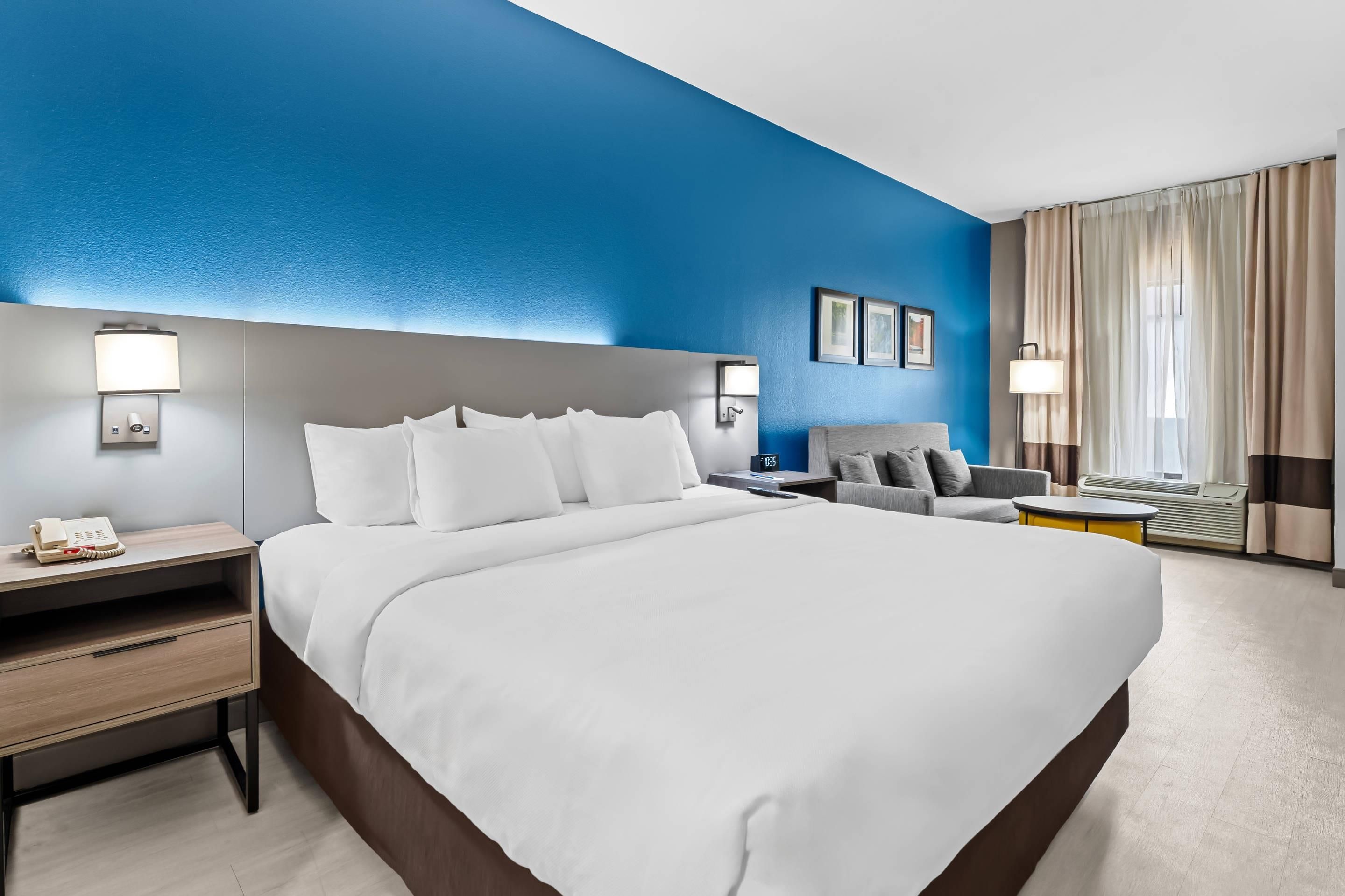 Une chambre d’hôtel avec un grand lit, des tables de chevet, une chaise, un bureau et une fenêtre avec des rideaux.