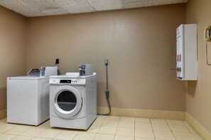 A laundry room with a front-loading washer and dryer, a utility box, and a phone on the wall. - Comfort Inn & Suites Perry National Fairgrounds Area (Perry)
