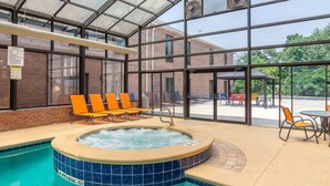An indoor swimming pool with a hot tub, surrounded by orange chairs and a covered patio area with tables and chairs. - Comfort Inn & Suites Perry National Fairgrounds Area (Perry)