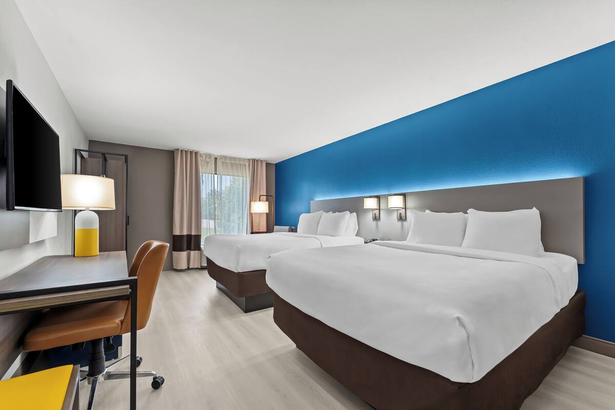A hotel room with two beds, a desk, a chair, and a TV.