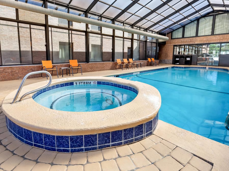 Una piscina interior con un jacuzzi, rodeada de sillas de descanso y un techo de cristal.