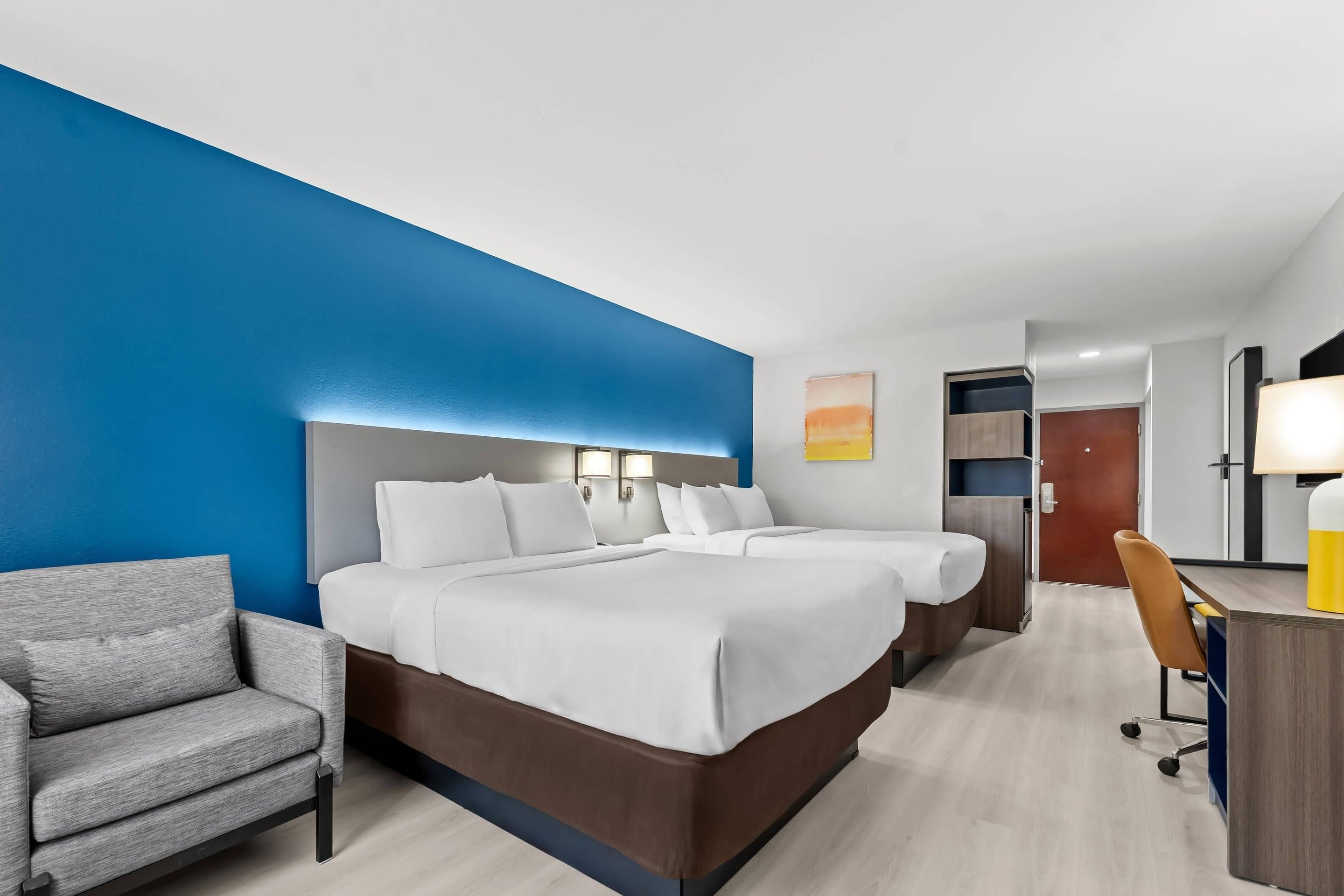 Una habitación de hotel con una cama grande, un escritorio, una silla y una pared azul decorativa.