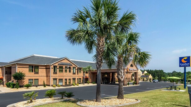 A hotel with a central entrance, palm trees, and a parking lot. - Comfort Inn & Suites Perry National Fairgrounds Area (Perry)