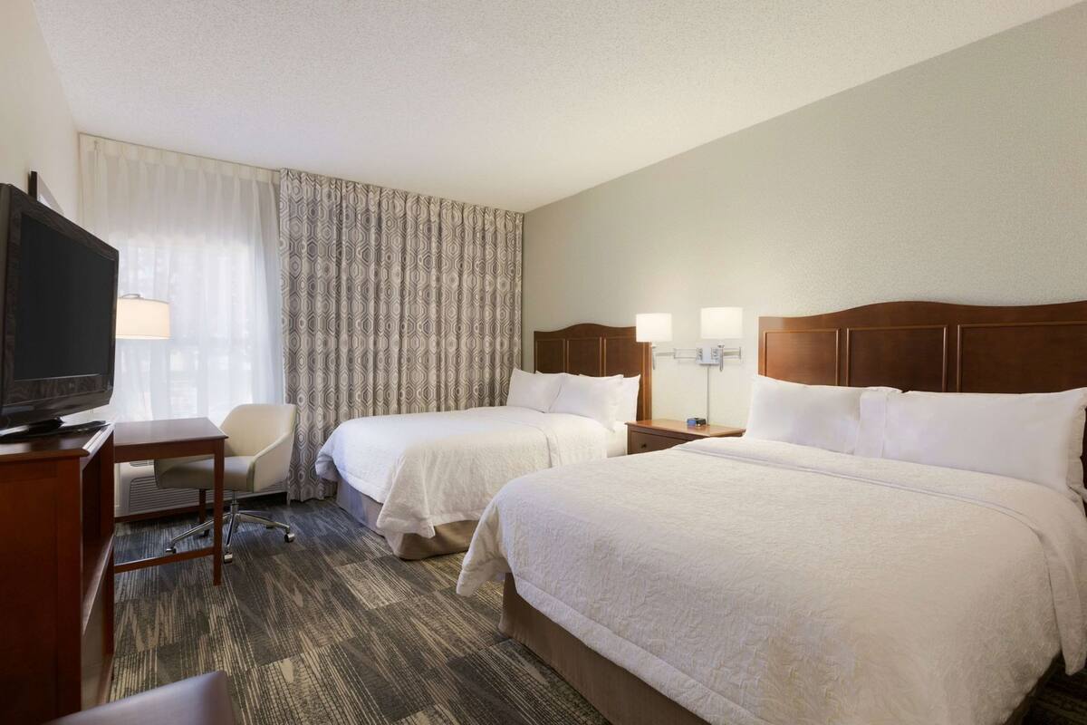 Ein Hotelzimmer mit zwei Betten, einem Fernseher, einem Schreibtisch und einem Stuhl.