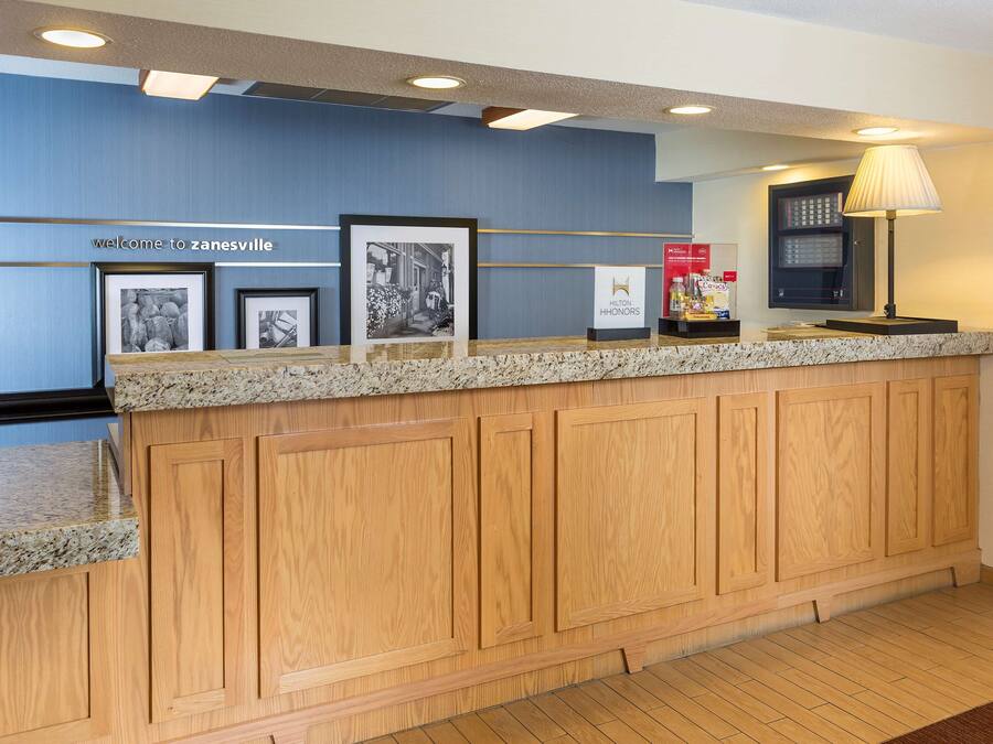 A reception area with a wooden counter, framed pictures, a welcome sign, a lamp, and a vending machine.