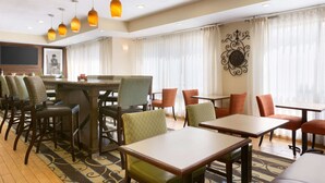 A hotel dining area with multiple tables and chairs, a television, and decorative wall art. - Hampton Inn Zanesville (Zanesville)