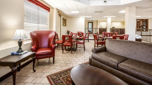 A spacious lobby with a red leather chair, a brown sofa, and a dining area with red chairs and tables.