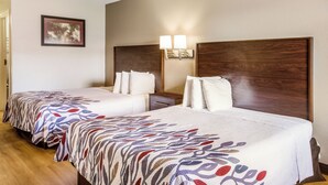 Een hotelkamer met twee bedden, een houten hoofdbord, een nachtkastje, een lamp en een lijst aan de muur.