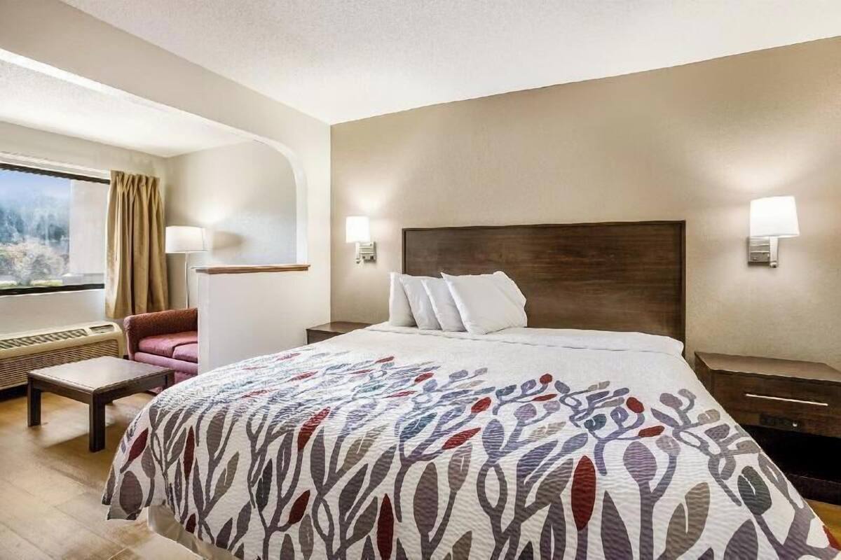 Habitación de hotel con una cama grande, una silla, un escritorio, una ventana con cortinas y lámparas fijadas a la pared.