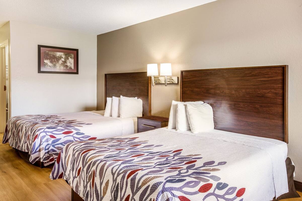 Una habitación de hotel con dos camas, una mesita de noche, una lámpara de pared y un cuadro en la pared.