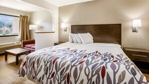 A hotel room with a large bed, a desk, a chair, a window with curtains, and two wall-mounted lamps.