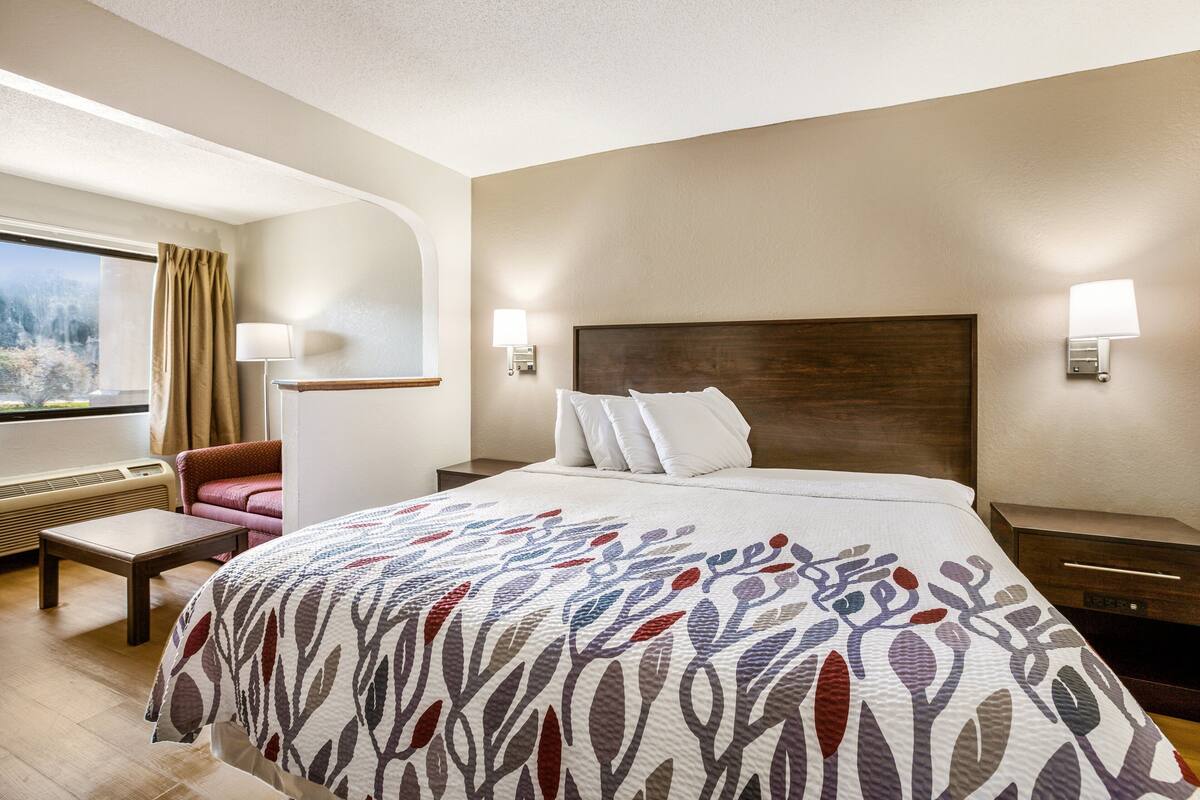Una habitación de hotel con una cama grande, un escritorio, una silla, un ventanal con cortinas y dos lámparas de pared.
