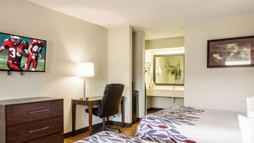 A hotel room with two beds, a desk, a chair, a TV, a mirror, and a dresser.