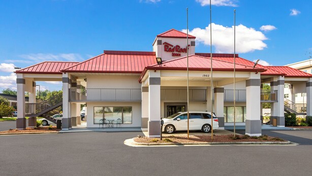 Un Red Roof Inn con techo rojo, estacionamiento techado y fachada blanca.