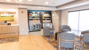 A hotel lobby with a reception desk, vending machines, seating area, and a large window. - Hampton Inn Williamsport-Downtown (Williamsport)