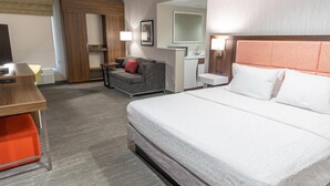 A hotel room with a bed, a sofa, a desk, a mirror, and a bathroom. - Hampton Inn Williamsport-Downtown (Williamsport)