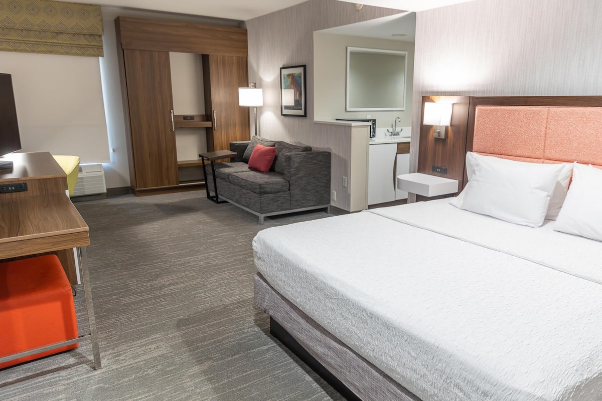 A hotel room with a bed, a sofa, a desk, a mirror, and a bathroom.