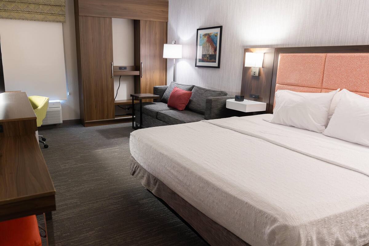A hotel room with a large bed, a desk, a chair, a lamp, and a painting on the wall.