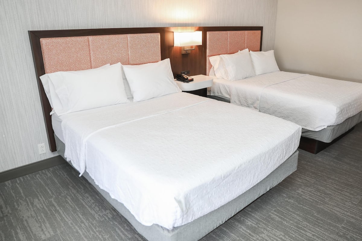 A hotel room with two beds, a nightstand, a lamp, and a telephone.