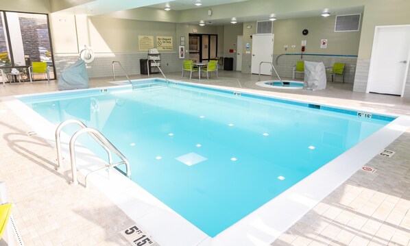 Una piscina interior con agua cristalina, una silla de salvavidas y una zona de estar con mesas y sillas.