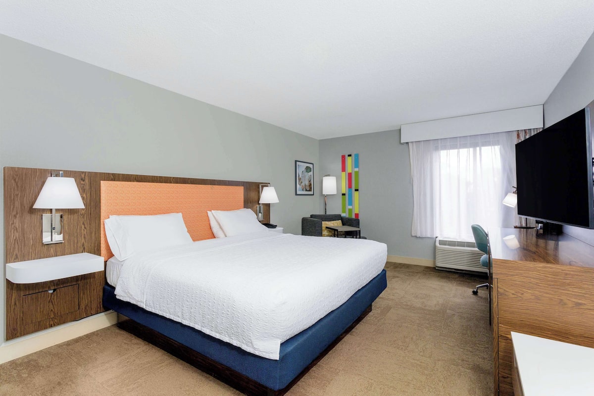 A hotel room with a large bed, bedside tables, a desk, and a TV.
