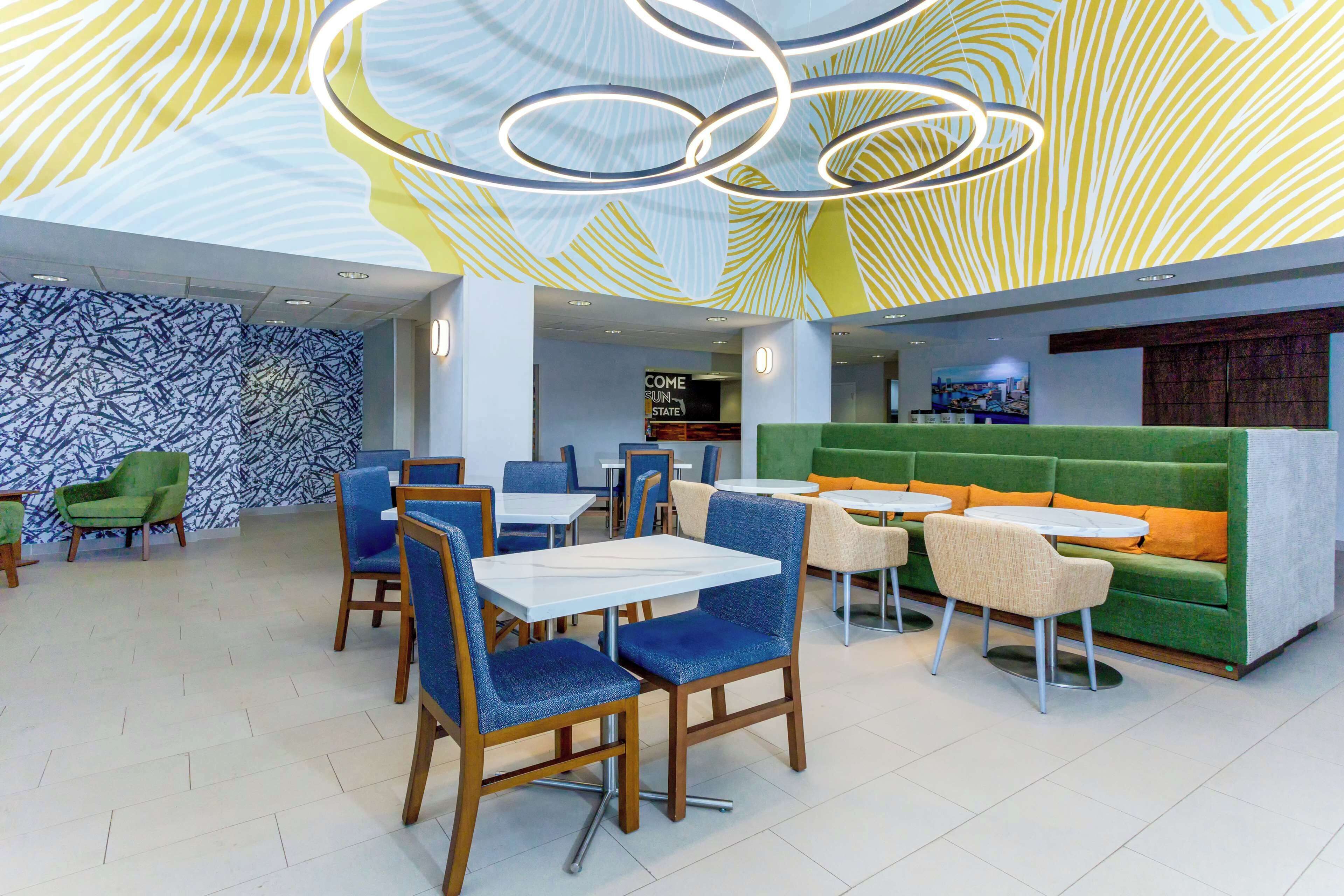 A modern restaurant with blue and green seating, a patterned ceiling, and a 'Come Sun State' sign.
