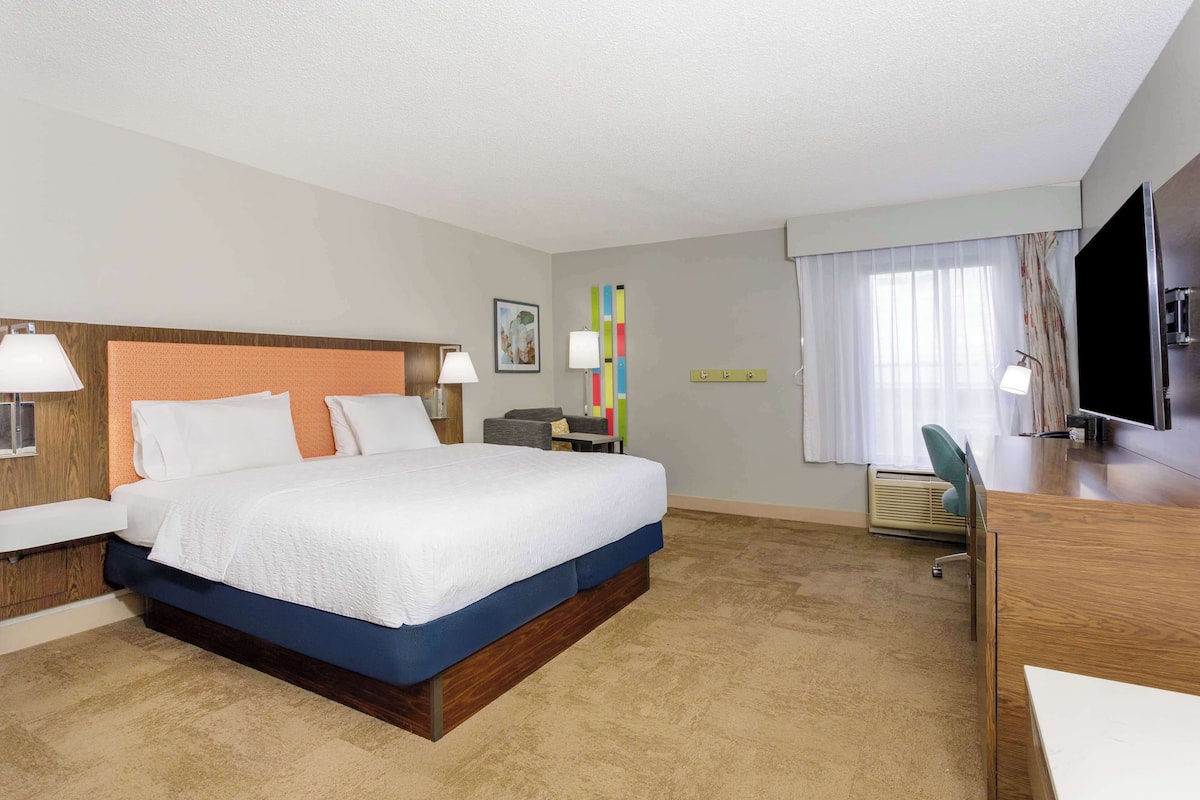 A hotel room with a bed, desk, TV, and a window with curtains.