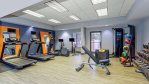Un gimnasio con cintas de correr, elípticas, un banco de pesas y varias pelotas de ejercicio.