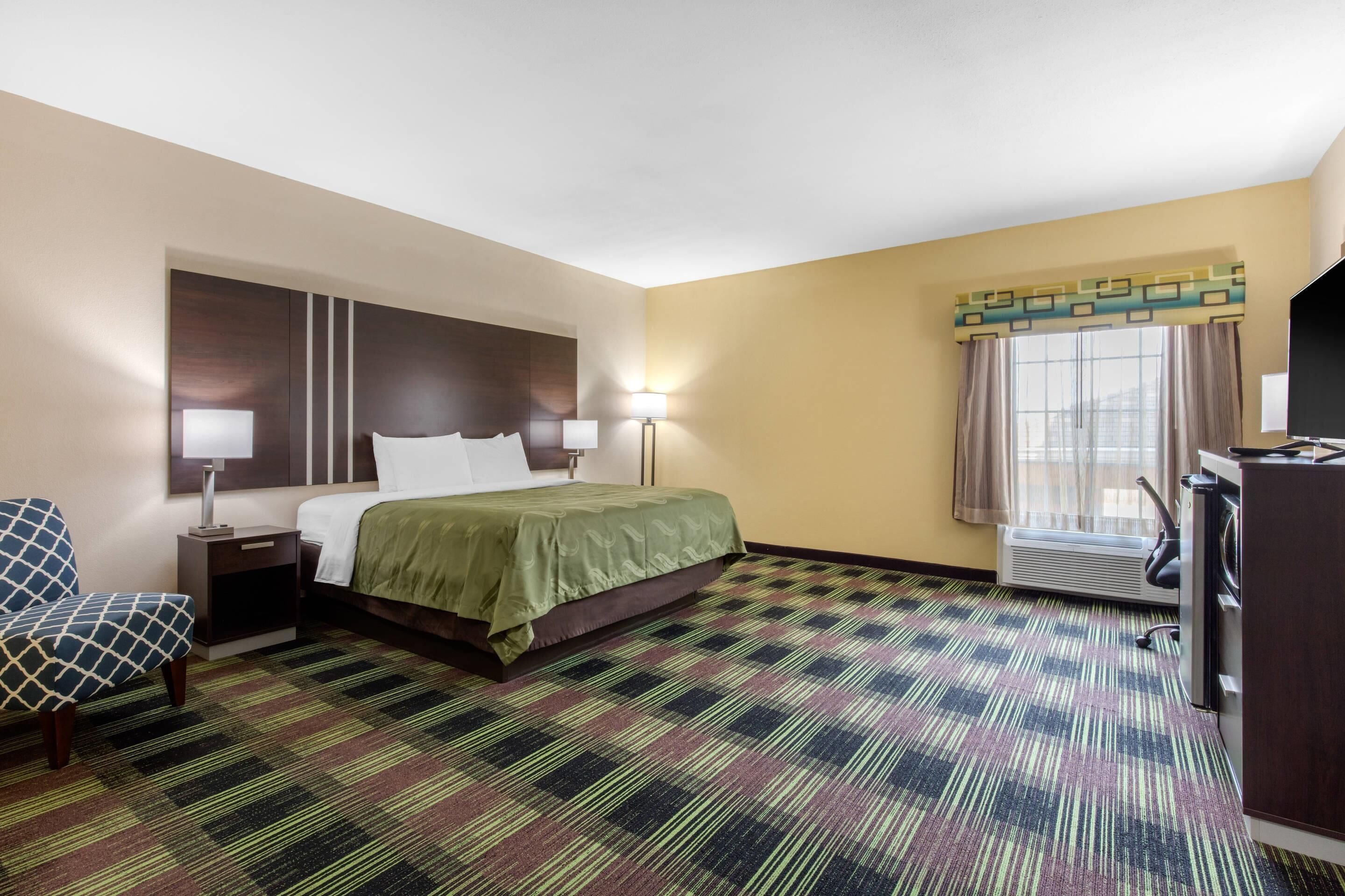 A hotel room with a bed, bedside lamps, a chair, a desk, and a window with curtains.