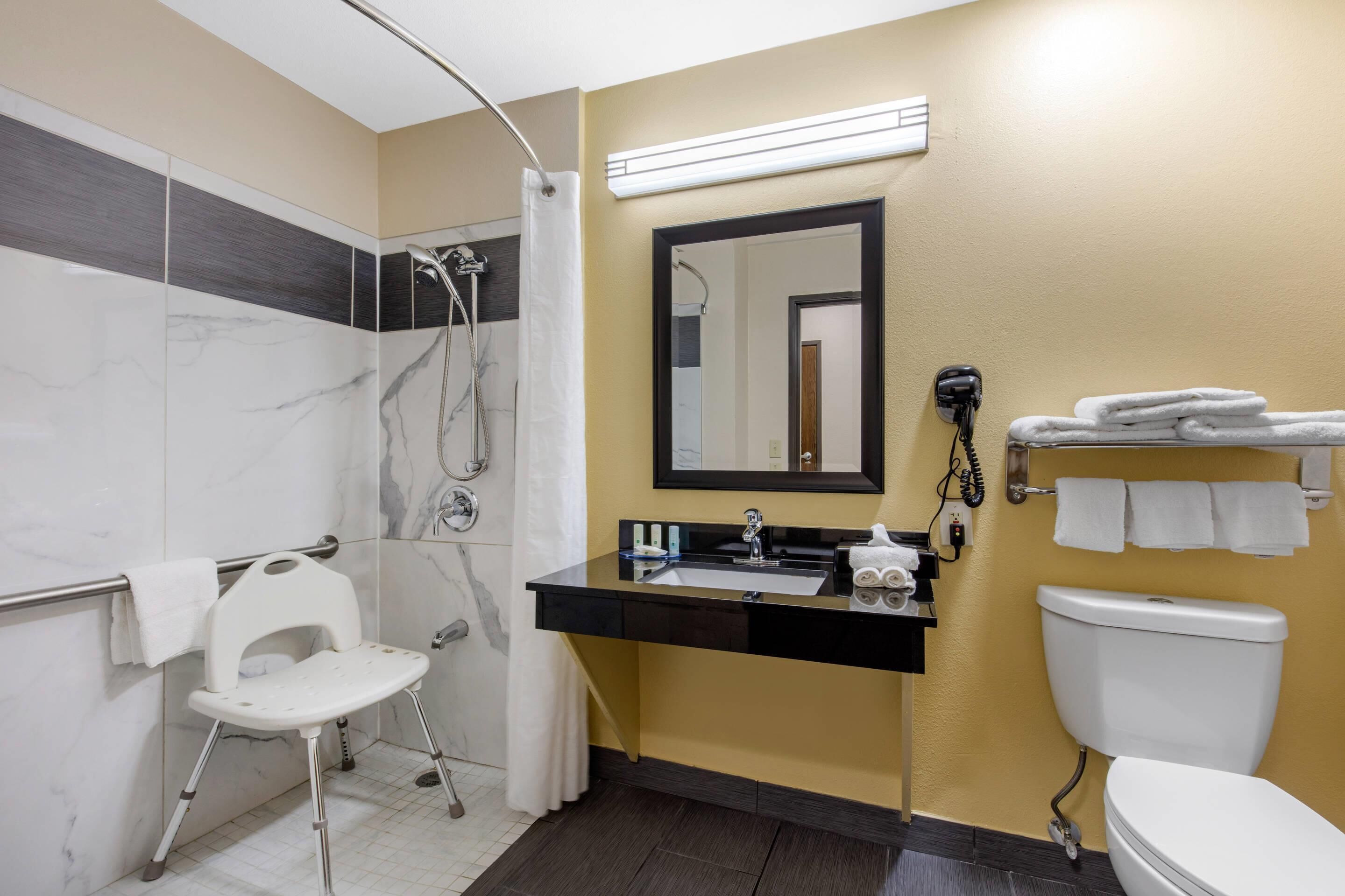 Une salle de bain équipée d’une douche, de toilettes, d’un lavabo, d’un miroir et d’une chaise.