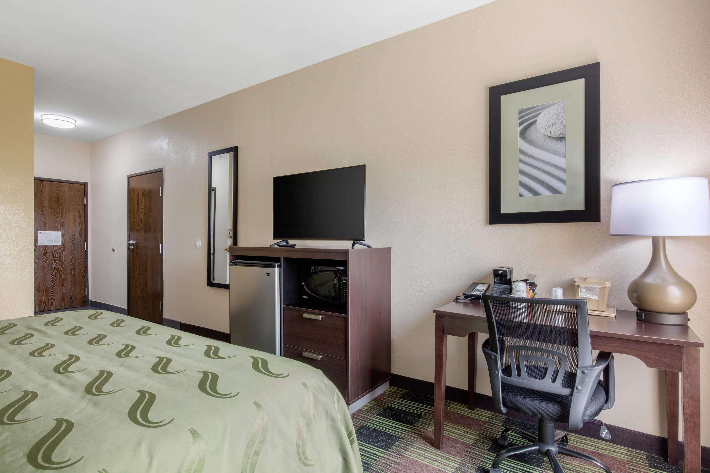A hotel room with a bed, desk, chair, television, microwave, and a framed picture on the wall.