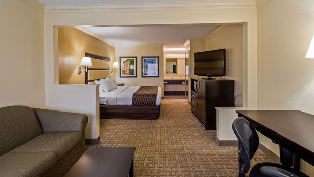 A hotel room with a bed, a desk, a TV, a sofa, and a mirror. - Best Western Inn & Suites (Byron)