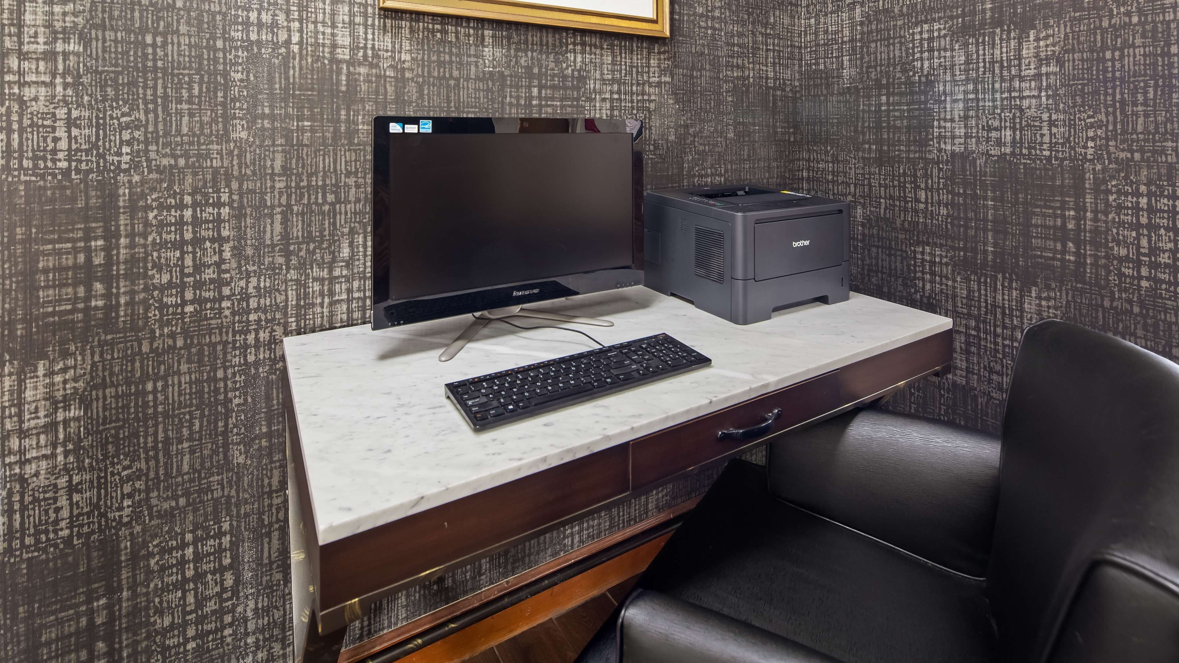 A desk with a computer monitor, keyboard, and printer in a room with patterned wallpaper.