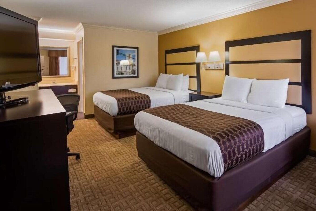 A hotel room with two beds, a desk, a chair, and a television.