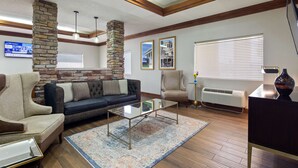 A living room with a stone accent wall, a dark blue sofa, a glass coffee table, and a beige armchair. - Best Western Inn & Suites (Byron)