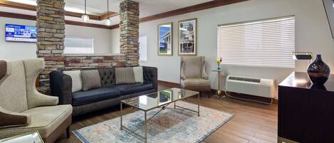 A living room with a stone accent wall, a dark blue sofa, a glass coffee table, and a beige armchair.
